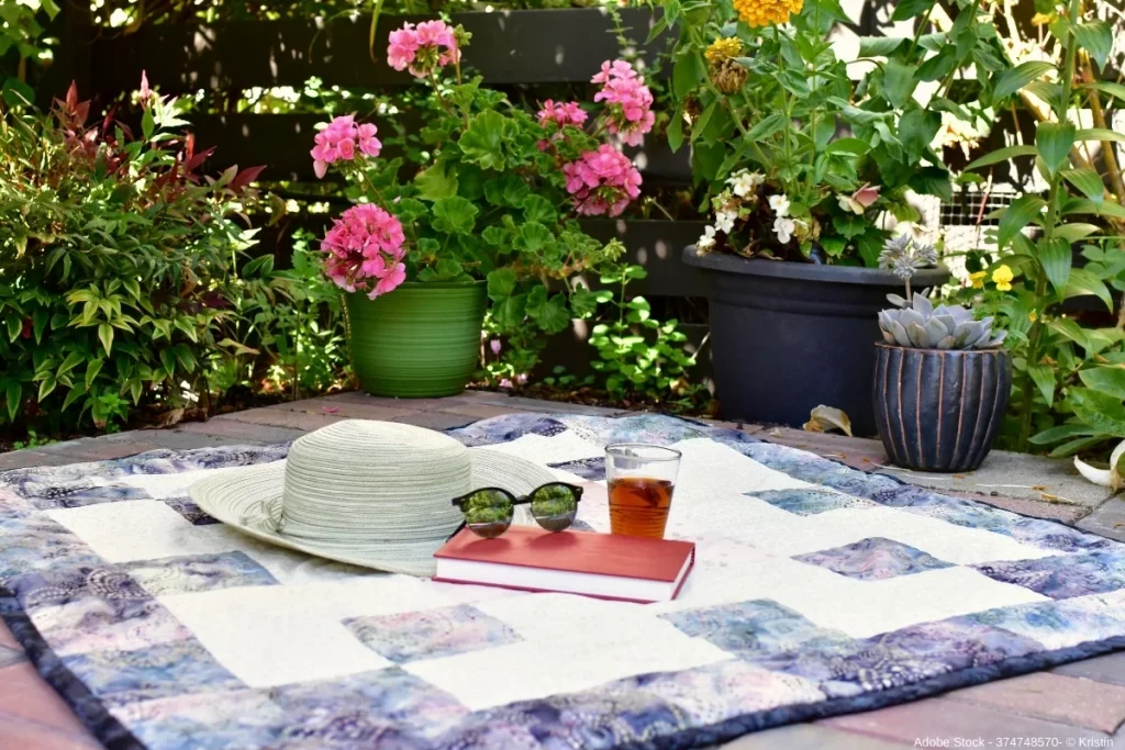 Picknickdecke im blühenden Garten mit Buch, Sonnenhut und Getränk, entspannte Sommeratmosphäre für eine gemütliche Staycation.